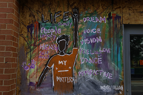 Painting of a person on a wall with raised fist in the air, surrounded by words of empowerment.
